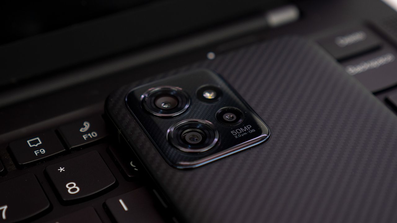 The camera island of the ThinkPhone by Motorola on a Lenovo ThinkPad Carbon X1 laptop