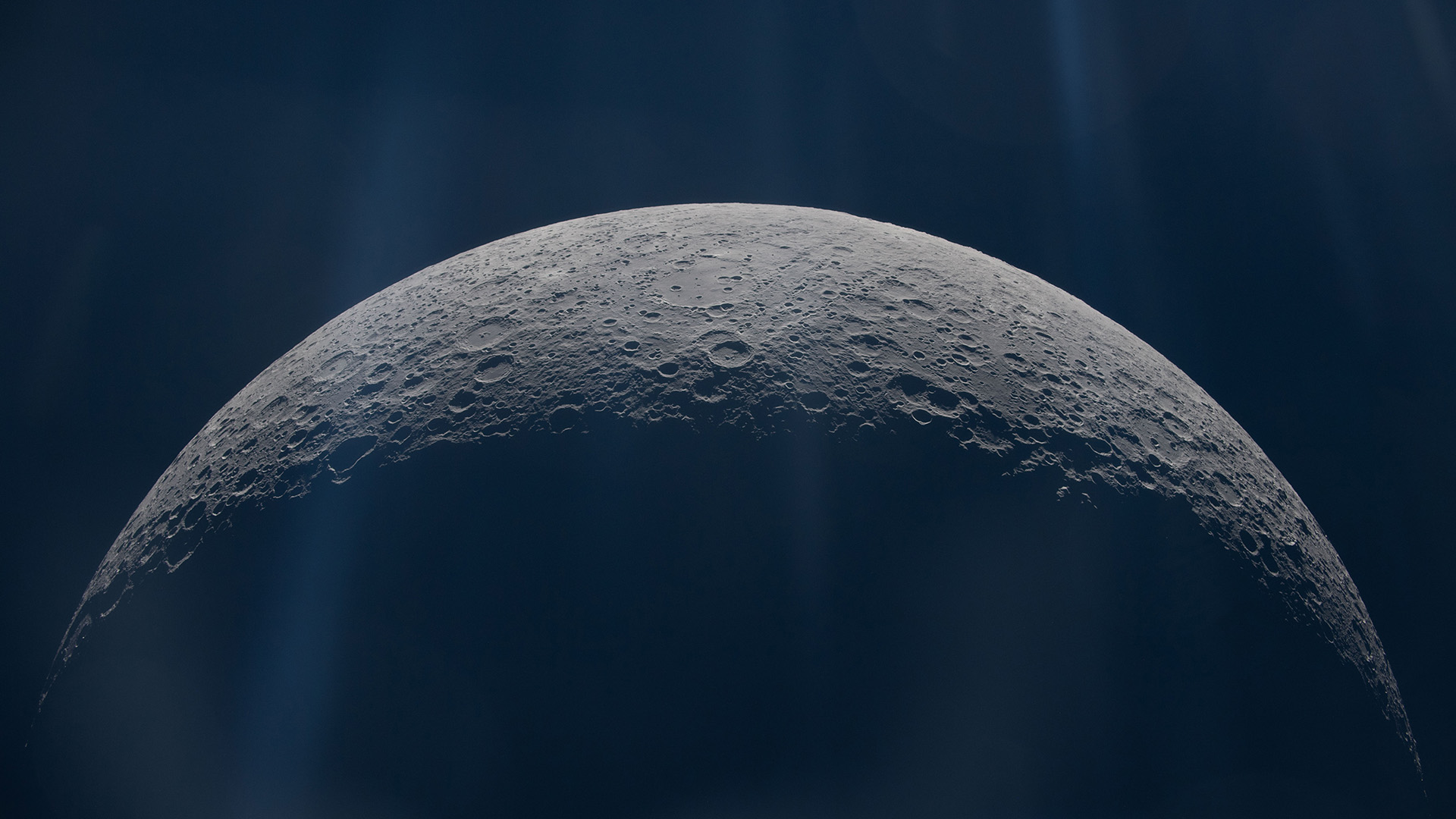 A close up of the moon's surface, showing its top half illuminated by glowing light from above.