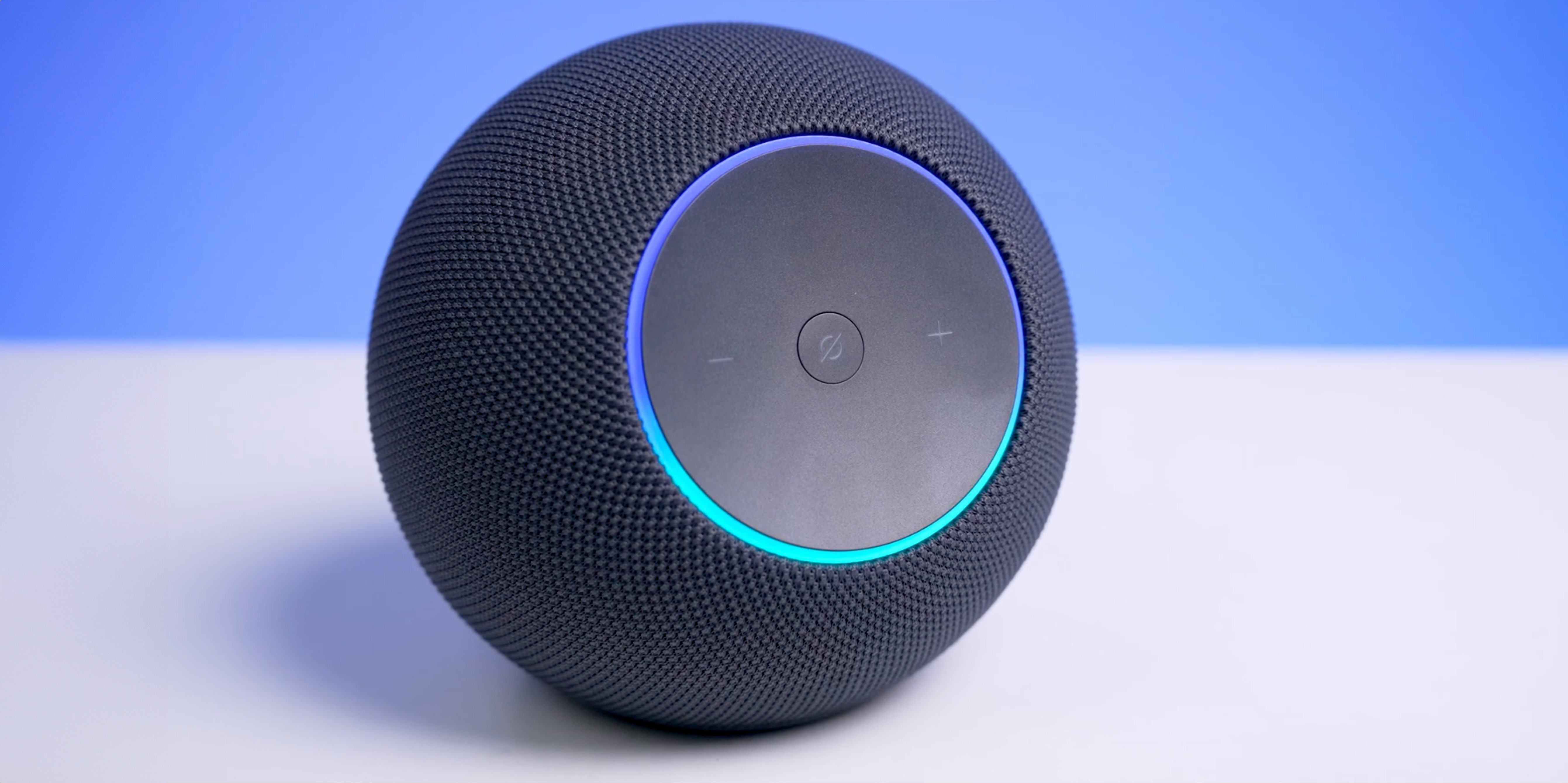 Echo Studio (2nd gen, 2025) on a white table with a blue background, Alexa ring illuminated blue