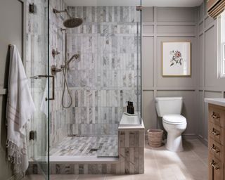A bathroom with a large walk-in shower clad with grey marble tiles, and a grey wall with millwork
