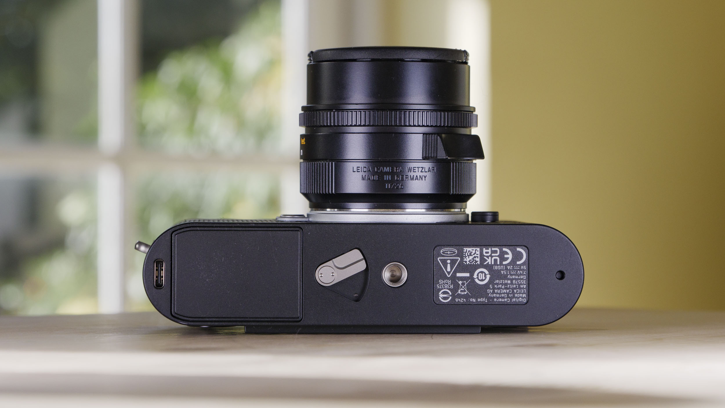 Underside of the Leica M EV1 camera, on a wooden table with glass-panelled door backdrop