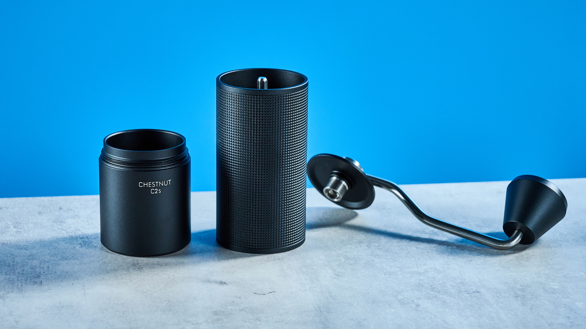 the timemore chestnut c2s coffee grinder in black showing its hand crank and catch chamber photographed against the blue tom's guide background