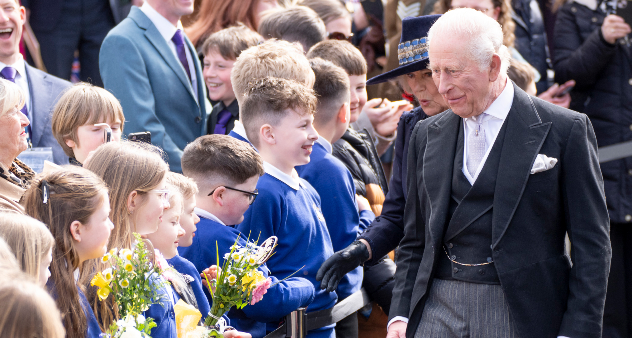 King Charles wearing a suit walking past a group of students