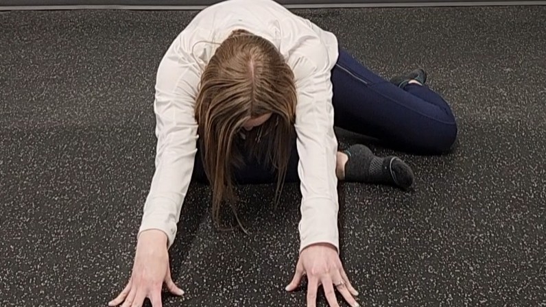 Woman demonstrating stretch. She wears a white long-sleeve top, blue sports leggings and black socks