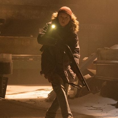 bella ramsey as ellie walking with a gun in a still from the last of us season 2