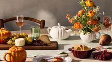 White tabletop with a wooden cheeseboard and white, orange and red stone pumpkin dishes