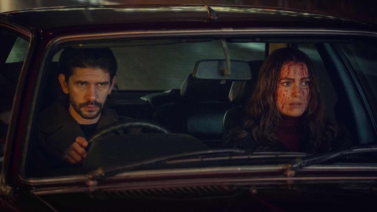 Sam and Helen sitting in a car looking shocked at something off camera. Helen&#039;s face is covered in blood.