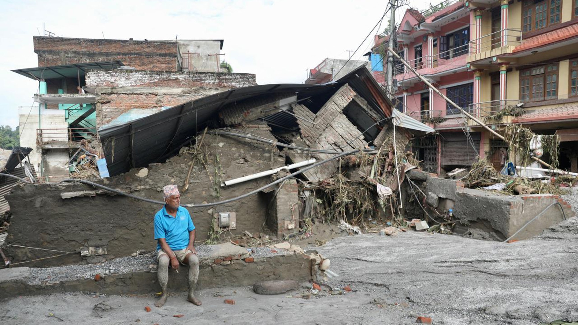 A local resident sits near a collapsed house lying deluged in sludge after flash floods at Devighat, Bidur Municipality in Nepal's Nuwakot district on August 27, 2026.