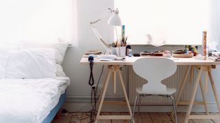 A desk is placed next to a bed in a white and neutral bedroom