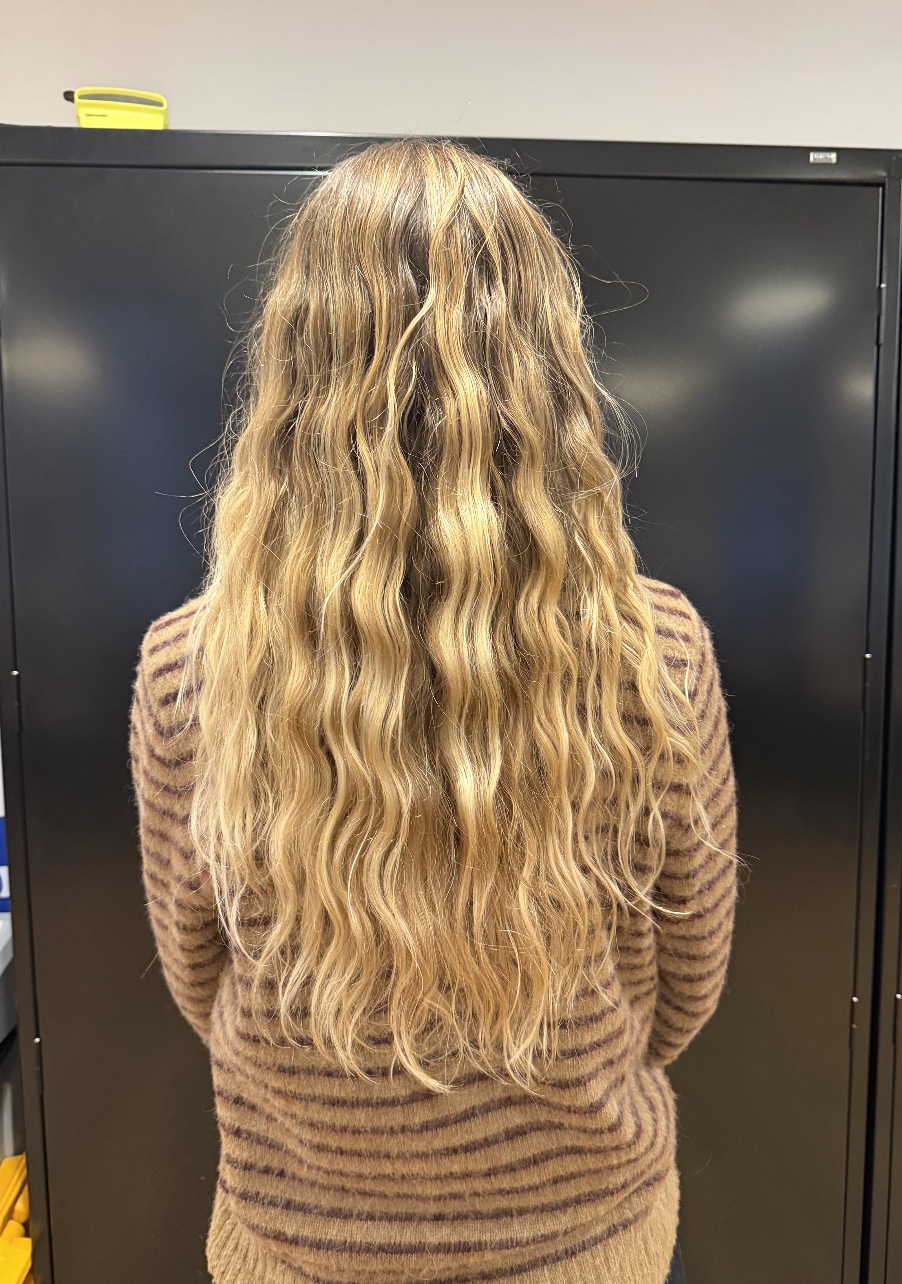 a blonde woman with long wavy hair in a striped sweater from the back