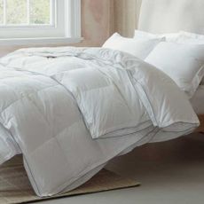 An all-seasons duvet on a bed with white pillows and bare plaster walls