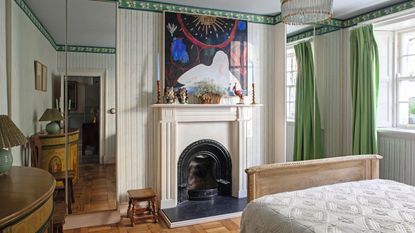 a large bedroom with a victorian fireplace, green and white striped walls with alcove closets with mirror fronts