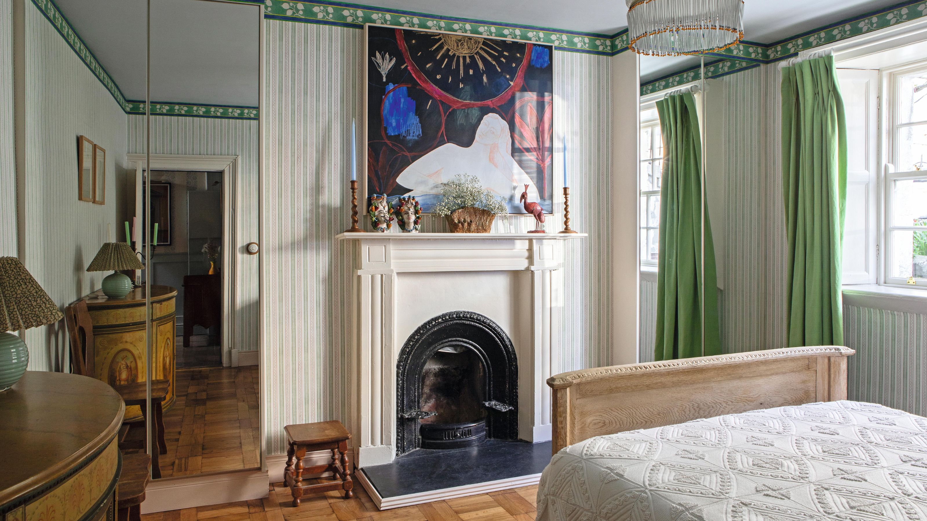 a large bedroom with a victorian fireplace, green and white striped walls with alcove closets with mirror fronts