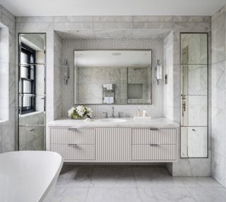 Bathroom with wall hung vanity and mirror above and mirrored cabinets alongside with neutral floor and wall tiles and bath