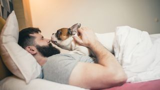 Dog giving man cuddle in bed