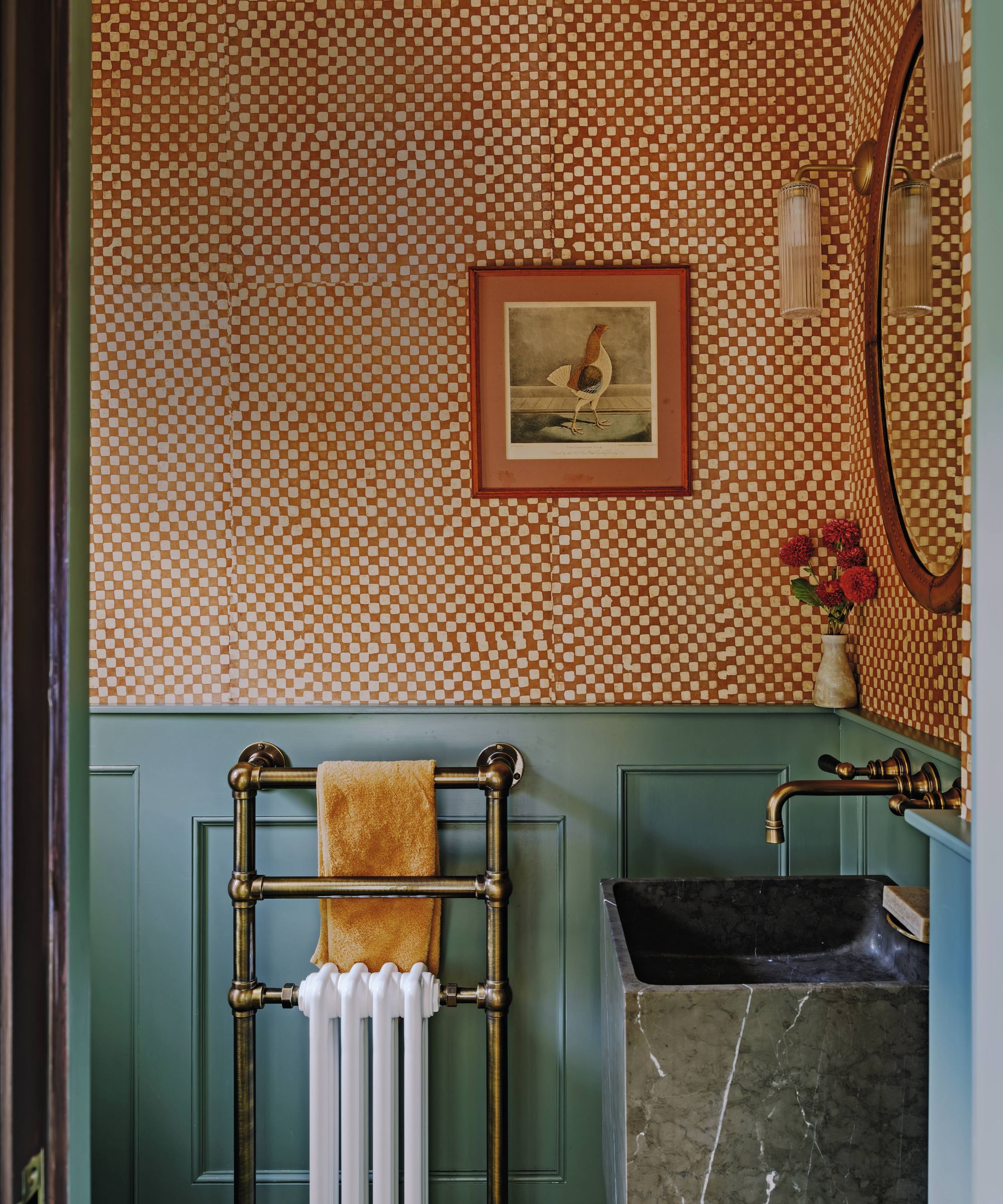a jewel box cloakroom with half height green blue paneling, checkerboard red gingham wallpaper and a marble sink