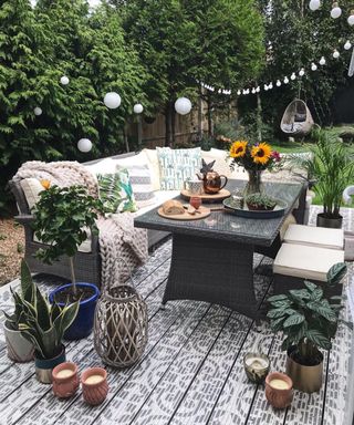 A deck idea with mosaic style stenciling, black rattan table, potted plants and candles, and egg chair in background