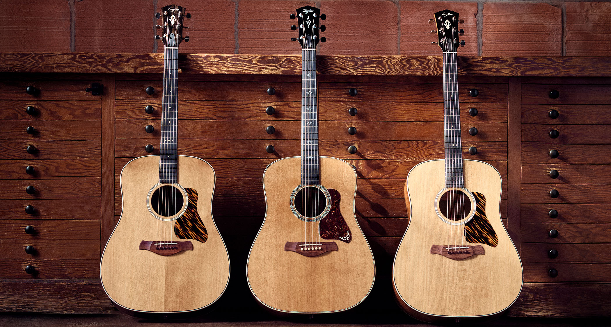 Three of Taylor's new Gold Label square-shouldered dreadnoughts are photographed in front of a vintage set of cabinets.
