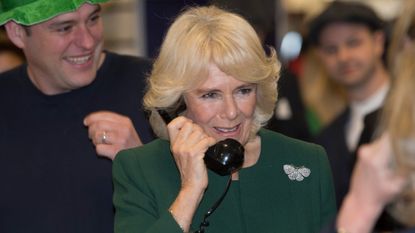 Queen Camilla talks on an old rotary phone while wearing a green dress