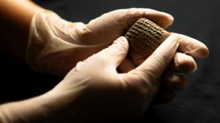 A cuneiform tablet on the hands of a person wearing gloves