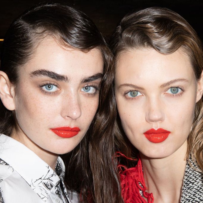 Two models with full brows wearing bright red lipstick