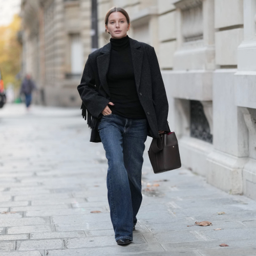 PARIS, FRANCE - OCTOBER 27: Diane Batoukina wears brown center parted hair styled in a low ponytail, a black wool blazer jacket with long fringe details along the sleeves by Balzac Paris layered over a black turtleneck sweater by The Frankie Shop, paired with straight blue denim jeans pants by Massimo Dutti, black leather pointed-toe boots by Mango, and a dark brown leather tote bag by Balzac Paris, during a street style fashion photo session, on October 27, 2025 in Paris, France. (Photo by Edward Berthelot/Getty Images)