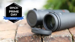 The Celestron Trailseeker 8x42 binoculars on a brick wall with one lens cap attached and one lens cap unattached showing the lens.