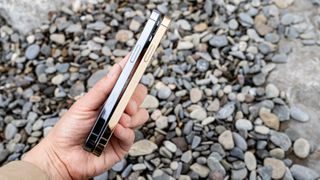 iPhone 12 Pro and iPhone 13 Pro being held together on pebble beach