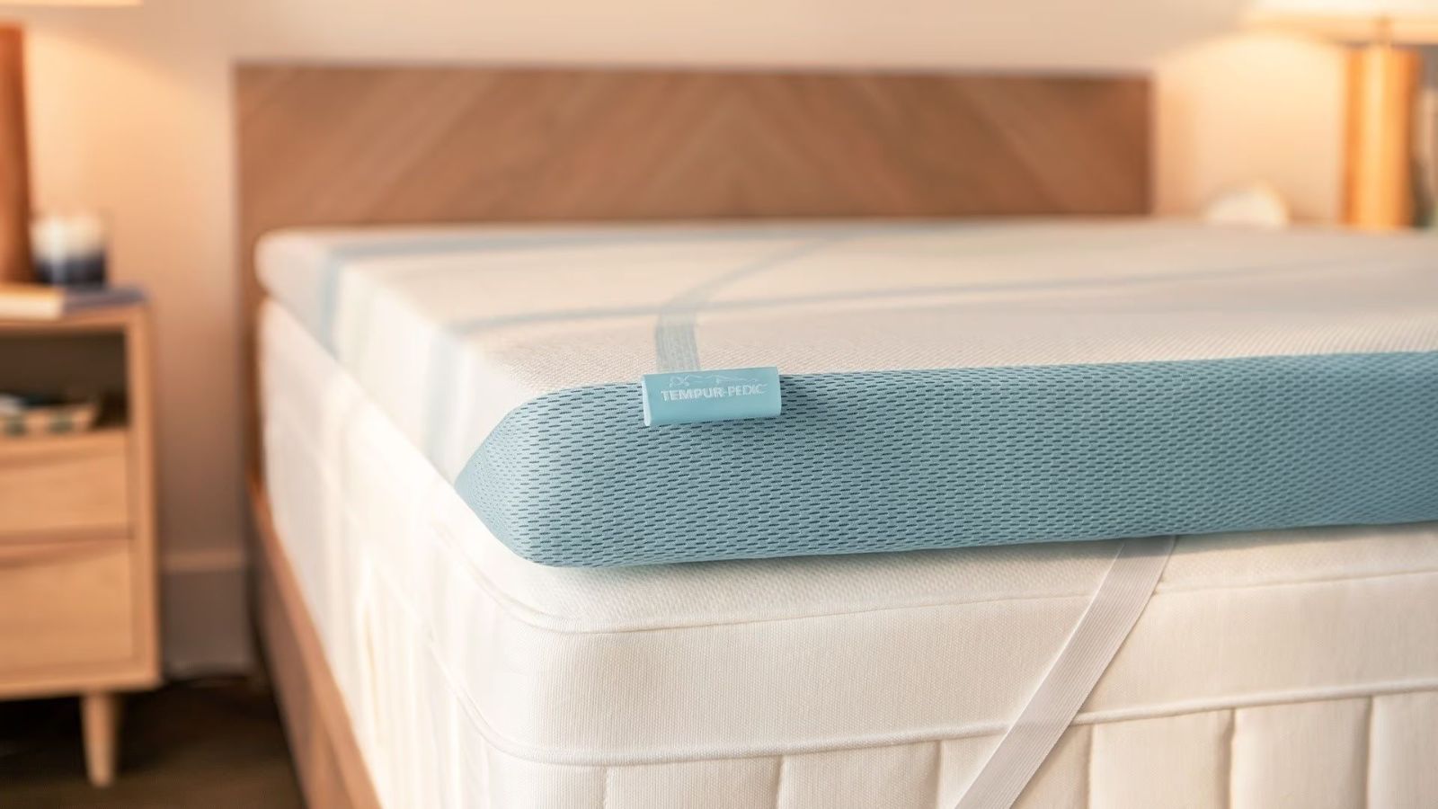 The corner of a Tempur-Pedic mattress topper on a mattress against white walls.