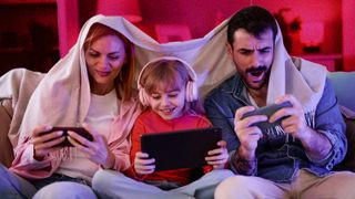 Young family sitting on sofa, all using phones and looking excited.