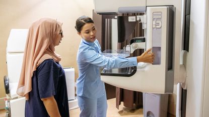 A doctor demonstrates a mammogram machine to a patient. 