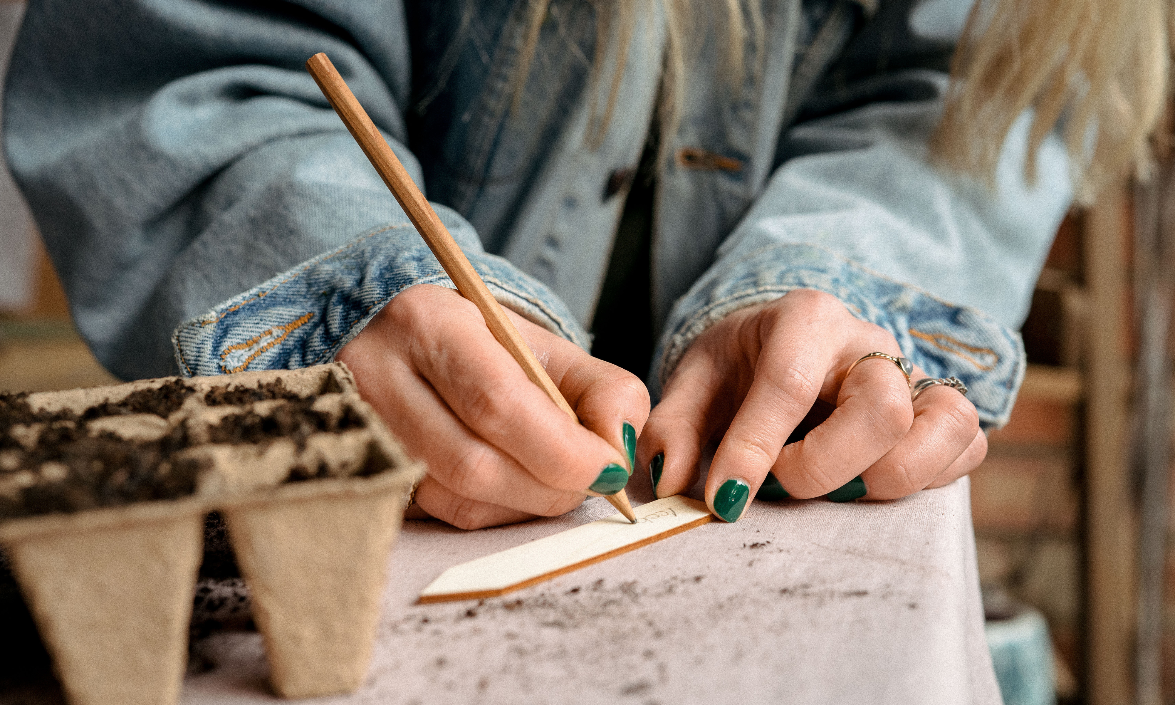 Hands writing on a wooden plant label with a pencil