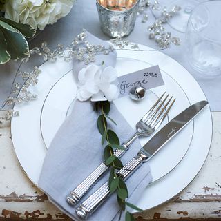 White dinner plate with foliage and white flower on napkin