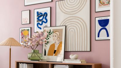 Small entryway color mistakes are a pain. Here is a pink wall with a gallery wall of colorful artwork and a brown console table and a lamp in front of it