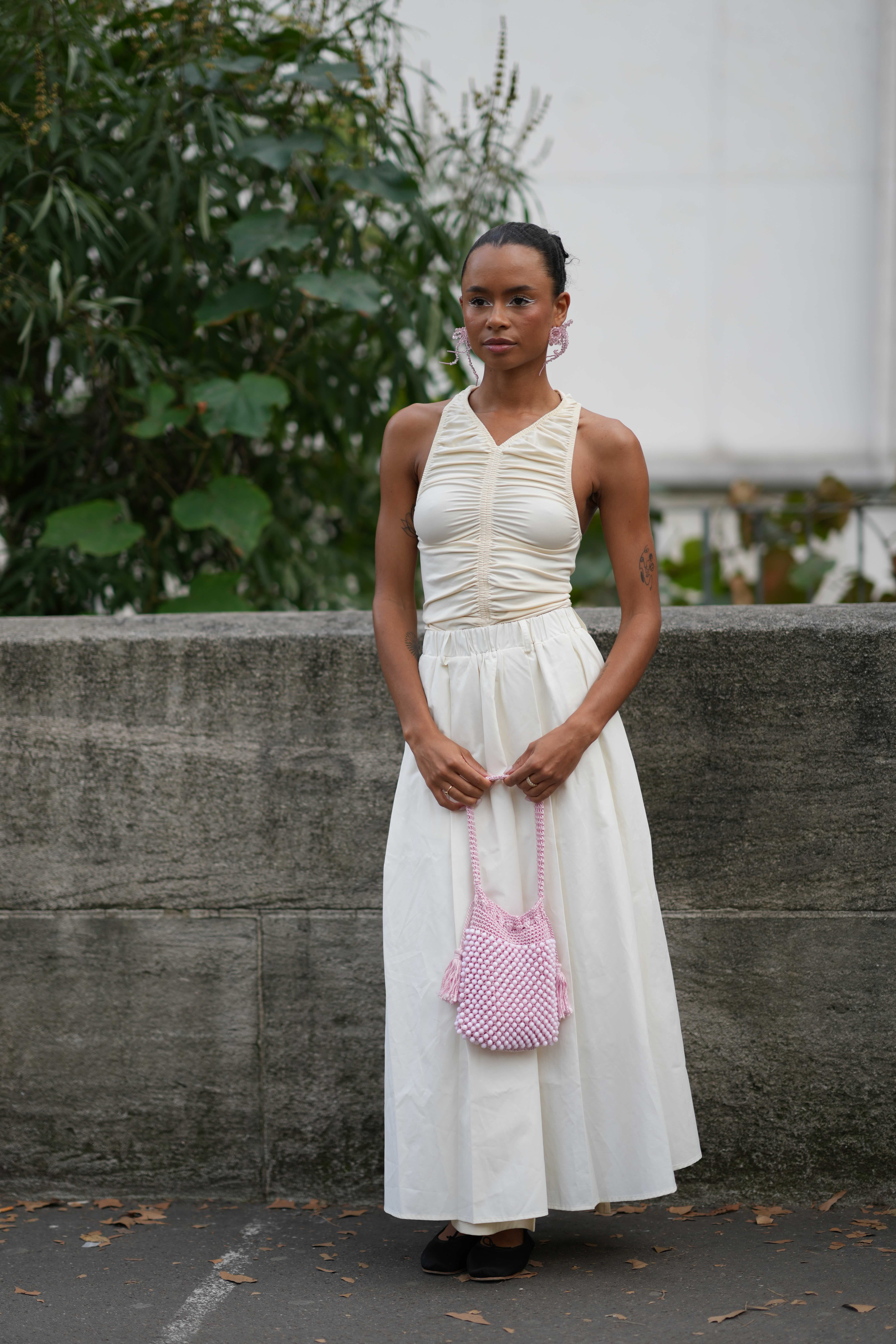 A guest wears a sleeveless gathered and pleated white dress, a pink beaded bag, outside Anrealage, during the Womenswear Spring/Summer 2024 as part of Paris Fashion Week on September 26, 2023 in Paris, France.