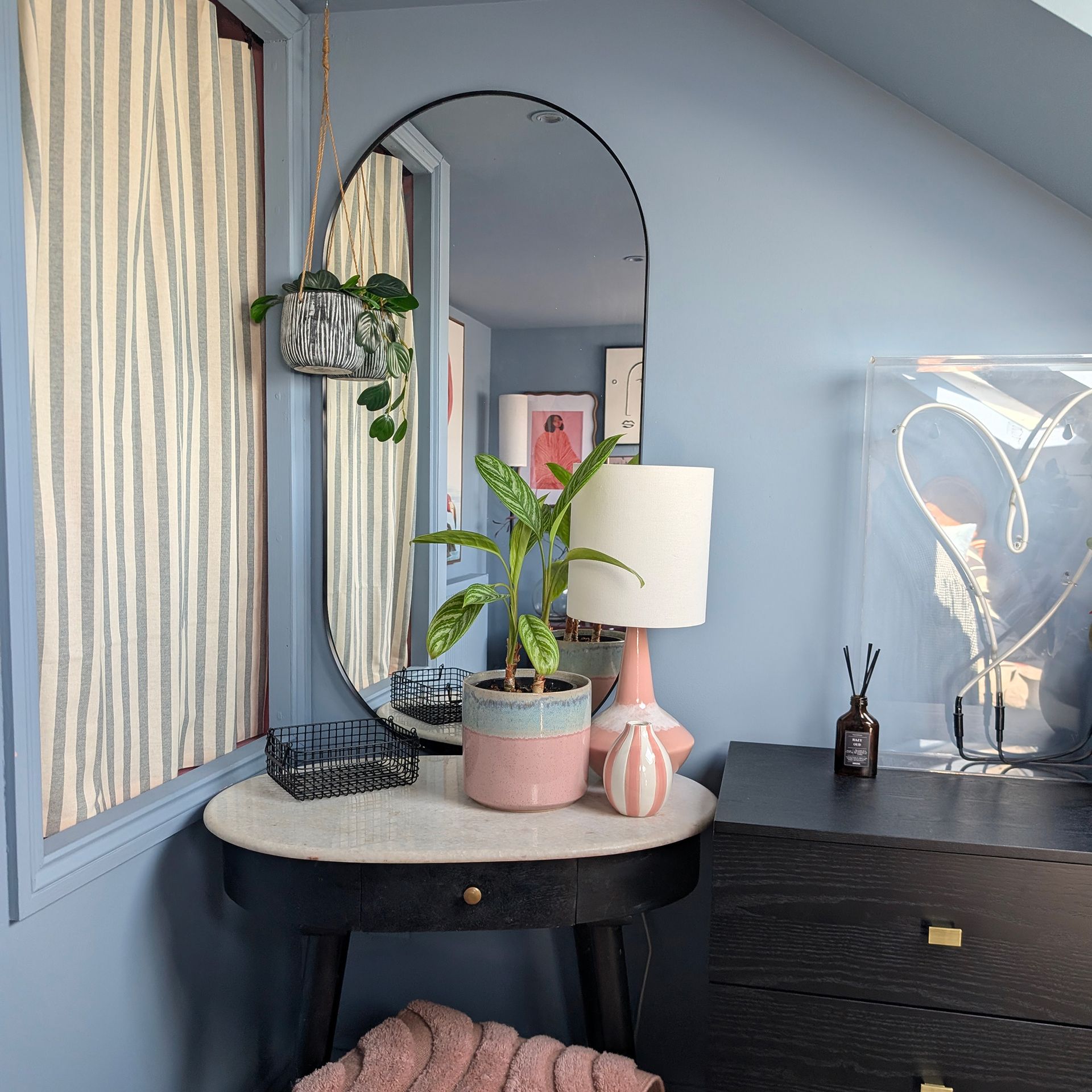 Blue bedroom with oval mirror over dressing table beside window covered with striped blind