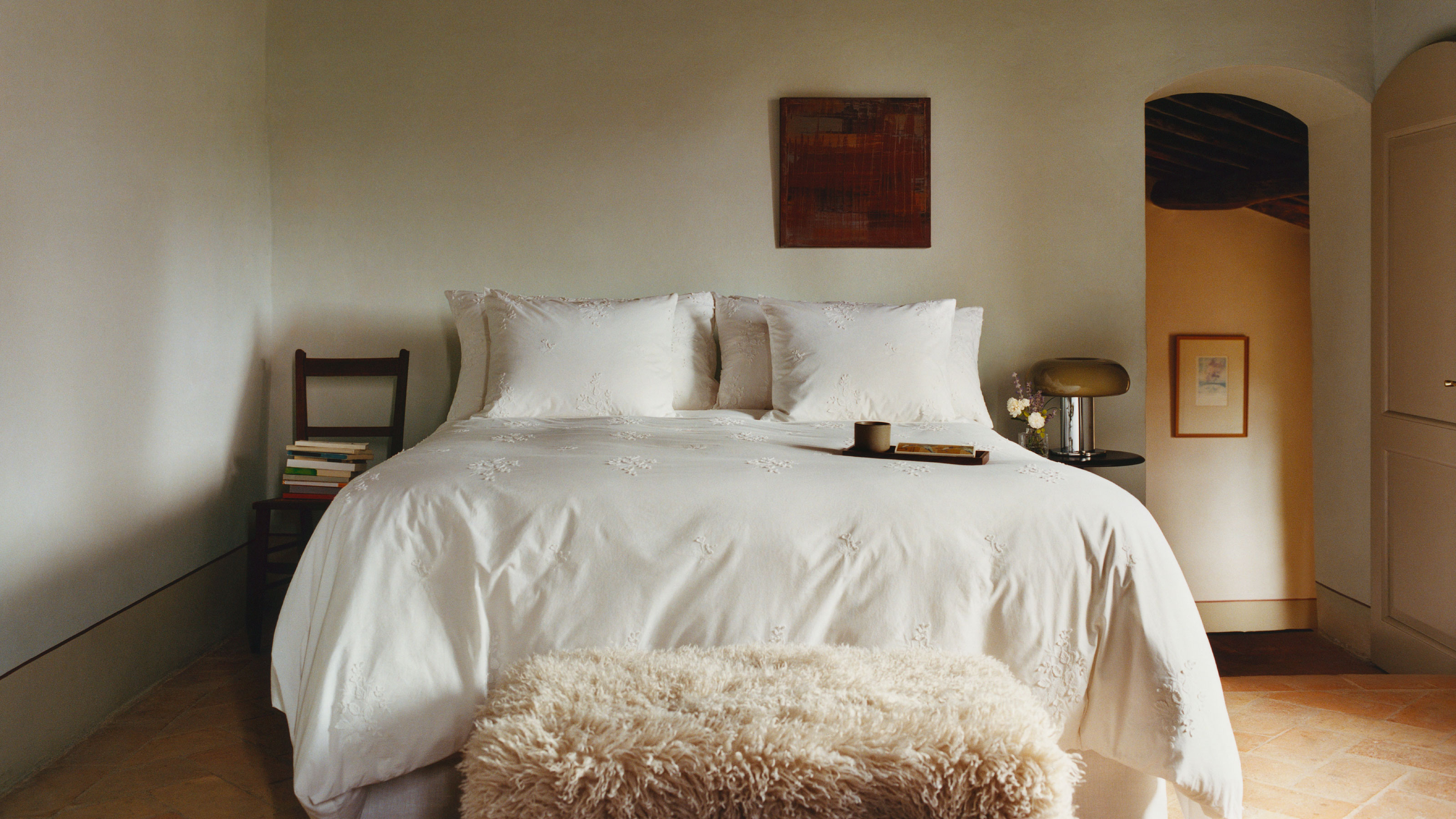 White bedroom with white bedding and fluffy footstool