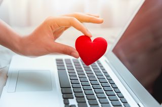 Hand holding felt heart over laptop
