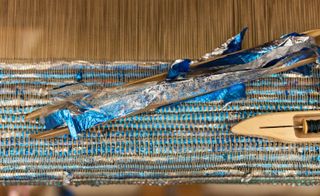 Close up shot of a recycled blue foil balloon being woven to make a tapestry, two wooden weave blocks. vintage loom