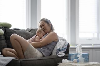 Woman lounging on a couch, snuggling her newborn baby.