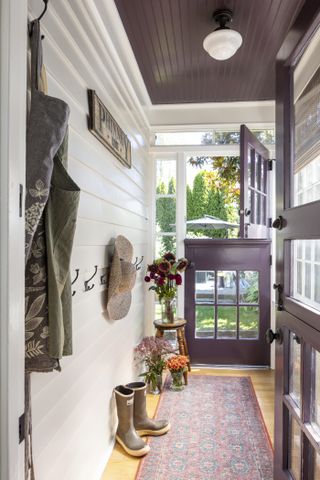 fall porch with plum and white color scheme, rug, wellies, pegs, small stool with flowers, aprons