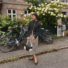 Alyssa wears maxi skirt and black long sleeve top with white and black handbag and black kitten heel shoes surrounded by flowers