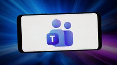 Logo and branding of Microsoft Teams application pictured on a smartphone screen, with blue and purple colors flashing in background.
