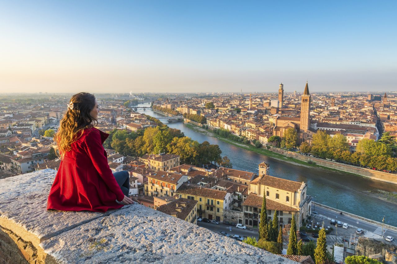 A woman in a red coat admires the view of Verona, Italy.