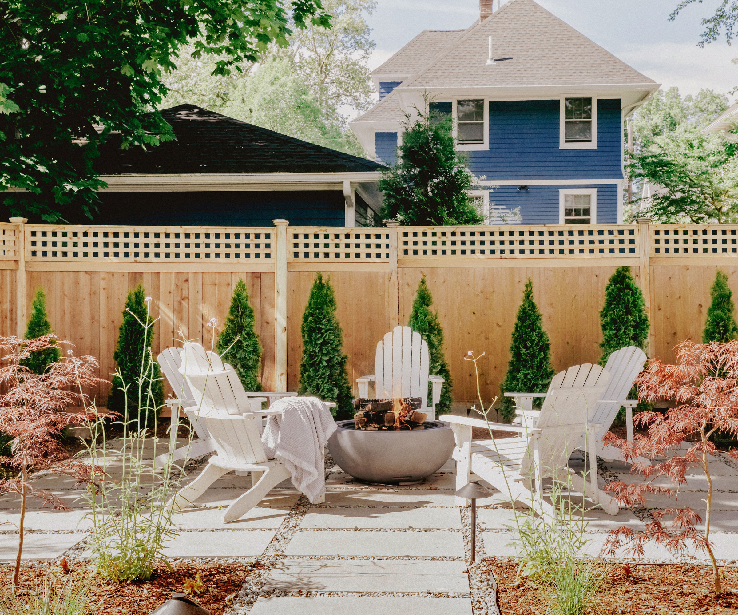fire pit and garden chairs with pavers, gravel and flowerbeds sparsely planted with airy plants and small acer trees