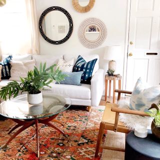 Boho style lounge with assorted round wall mirrors, shibori scatter cushions on sofa, global inspired feature rug, and mid-century modern glass and wood combo round coffee table.