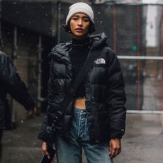 Fashion week attendee wears north face puffer jacket, grey beanie, and jeans
