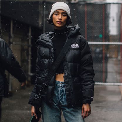 Fashion week attendee wears north face puffer jacket, grey beanie, and jeans 