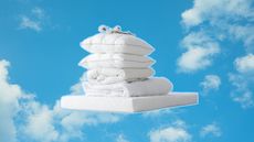 A cloudy blue sky background with a white mattress and a pile of bedding products stacked on top
