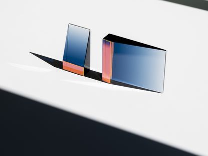 Two triangular shaped glass objects by John Hogan, reflecting light in pink and blue